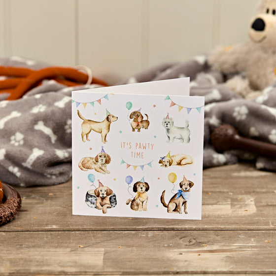 Greeting card with illustrations of dogs and text 'It's pawty time' on a wooden surface.