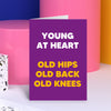 Tall, purple and bold. A hilarious birthday card perfect to bring a smile to your friends's face. Bright and big text reads 'Young at heart, old hips, old back, old knees'. A perfect funny birthday card. Dean Morris.