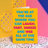 Hilarious, funky, gender neutural birthday card; blank inside; a bright yellow card; with courful, bold blue and pink text that reads 'You're at the age where you can laught, fart, sneeze and wee all at the same time'; by Dean Morris. 