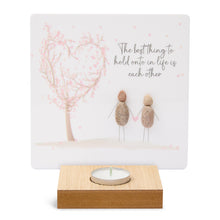  These wood t-light candle holders feature lovely artwork and sentimental messages. The candle burns in front of the printed artwork illuminating the message.&nbsp;

The artwork here depicts a pink cherry blossom tree blown in to the shape of a heart with 2 pebble art people holding hands. The message reads The best thing to hold onto in life is each other.