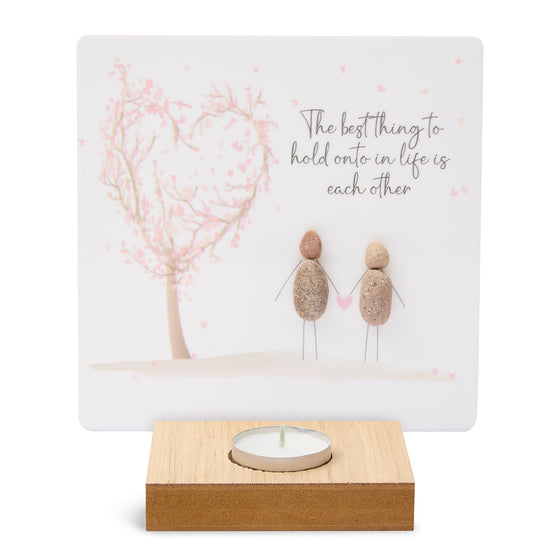 These wood t-light candle holders feature lovely artwork and sentimental messages. The candle burns in front of the printed artwork illuminating the message.&nbsp;

The artwork here depicts a pink cherry blossom tree blown in to the shape of a heart with 2 pebble art people holding hands. The message reads The best thing to hold onto in life is each other.