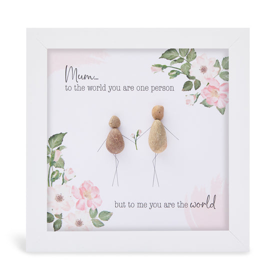 This white shadowbox framed pebble art print features a mother and daughter exchanging flowers and has a floral motif design.&nbsp;It reads Mum to the world you are one person but to me you are the world.