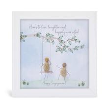  This white shadowbox framed pebble art print features someone on swing hanging from a tree with someone else pusing them.&nbsp;It reads "Here's to love, laughter and happy ever after! Happy Engagement!