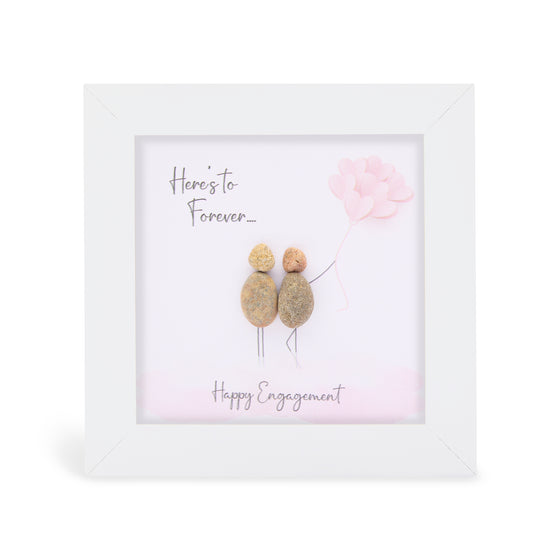 These small white shadow box frame gifts are made with a 4-inch white shadow box frame with a plexiglass insert, helping it be less fragile in the post and around the home. You can also easily take them apart to clean the inside of the glass or frame if you need to. They come individually boxed for added protection during shipping.

This white shadowbox framed pebble art print features 2 people holding a bouque of pink balloons. It reads Here's to Forever! Happy Engagment.