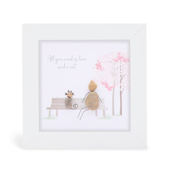 These small white shadow box frame gifts are made with a 4-inch white shadow box frame with a plexiglass insert, helping it be less fragile in the post and around the home. You can also easily take them apart to clean the inside of the glass or frame if you need to. They come individually boxed for added protection during shipping.

This white shadowbox framed pebble art features a person sitting on a bench with a cat. It reads All you need is love and a cat.