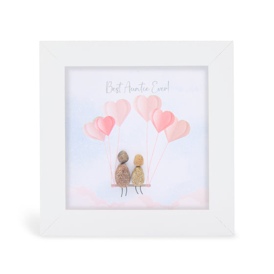 These small white shadow box frame gifts are made with a 4-inch white shadow box frame with a plexiglass insert, helping it be less fragile in the post and around the home. You can also easily take them apart to clean the inside of the glass or frame if you need to. They come individually boxed for added protection during shipping.

This white shadowbox framed pebble art print 2 people sitting in a swing with pink balloons overhead. It reads Best Auntie Ever.