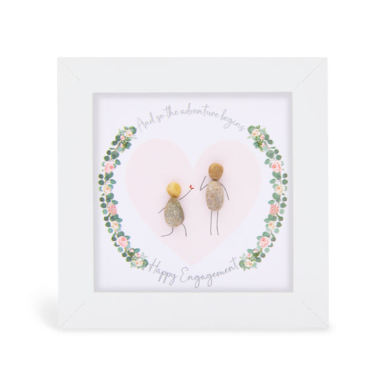 These small white shadow box frame gifts are made with a 4-inch white shadow box frame with a plexiglass insert, helping it be less fragile in the post and around the home. You can also easily take them apart to clean the inside of the glass or frame if you need to. They come individually boxed for added protection during shipping.

This white shadowbox framed pebble art features a couple inside a floral wreath design. It reads And so the adventure begins Happy Engagement